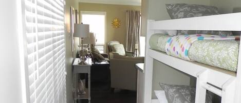 A narrow hallway with a bunk bed on the right, a chair in the center, and a lamp on a nightstand.