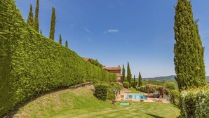 Une maison avec une piscine, entourée de haies soigneusement taillées et de grands arbres.
