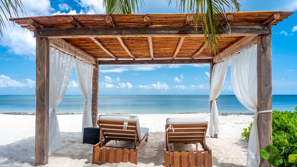 Una cabaña de madera en la playa con cortinas blancas y dos sillones de madera.