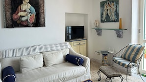 Ein Wohnzimmer mit einer Couch, einem Fernseher, einem Sessel und zwei Wandregalen mit Dekoration.