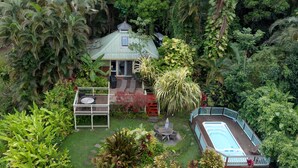 A house surrounded by lush greenery, a swimming pool, and a patio area with outdoor furniture. - Romantic Cottage, Private Acre of Paradise, View! Pool! (Hanalei)