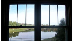 A room with a large window offering a view of a lake, a road, and a grassy area. - Mammaw's Lakefront Cabin bordering The Blue Ridge Parkway (Jefferson)