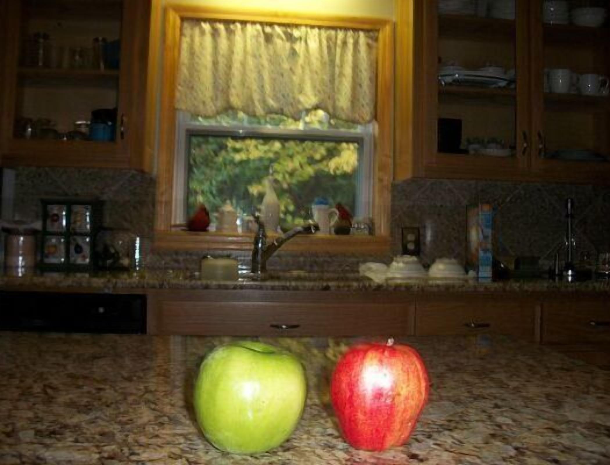 A kitchen with a window, a sink, and two apples on the counter.