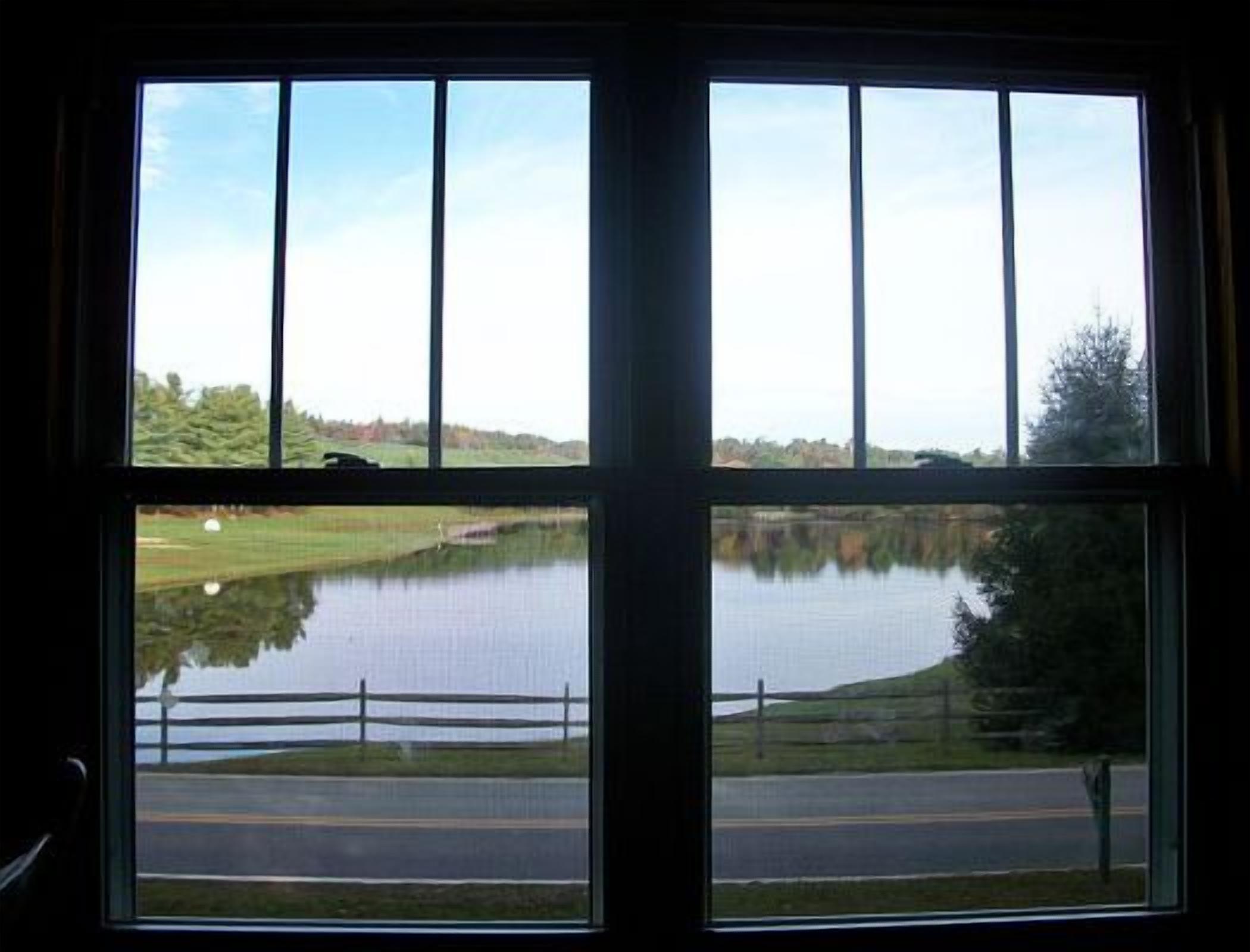 A room with a large window offering a view of a lake, a road, and a grassy area.