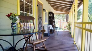 A wooden deck with a glass table and chairs, a rocking chair, and a vase of flowers. - Fivespot Cabin, an art and nature lover's retreat (Pinehurst)