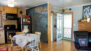 A cozy kitchen with a chalkboard wall, wooden cabinets, and a dining area with a table and chairs. - Fivespot Cabin, an art and nature lover's retreat (Pinehurst)