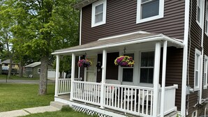 Une maison avec un porche, des balustrades blanches et des jardinières suspendues.