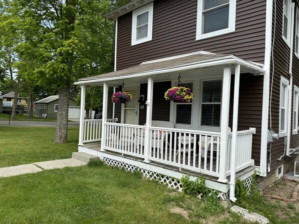 A house with a porch, white railings, and hanging flower baskets. - Falcon's Nest—Beautiful In-Town Bar Harbor Home, Walk to Downtown, Pet Friendly (Bar Harbor)