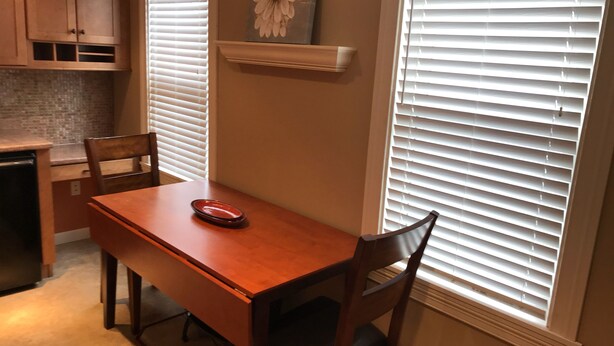 Un coin repas avec une table et des chaises en bois, une assiette rouge et une décoration florale au mur.