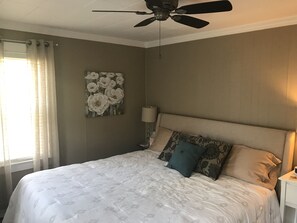 A bedroom with a bed, a ceiling fan, a wall-mounted lamp, and a floral artwork. - Falcon's Nest—Beautiful In-Town Bar Harbor Home, Walk to Downtown, Pet Friendly (Bar Harbor)