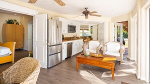 A spacious living area with a wooden coffee table, wicker chairs, a kitchen with white cabinets, and a ceiling fan. - Gulf Breeze (Naples)