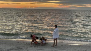 A beach scene with a sunset, calm sea, and people playing on the sand. - Gulf Breeze (Naples)