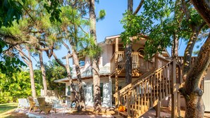 A two-story house with a wooden staircase, outdoor seating area, and a large tree in the foreground. - Gulf Breeze (Naples)