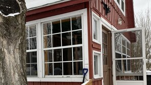 Une maison en bois rouge avec des fenêtres à cadre blanc, un porche en bois et un sol recouvert de neige.
