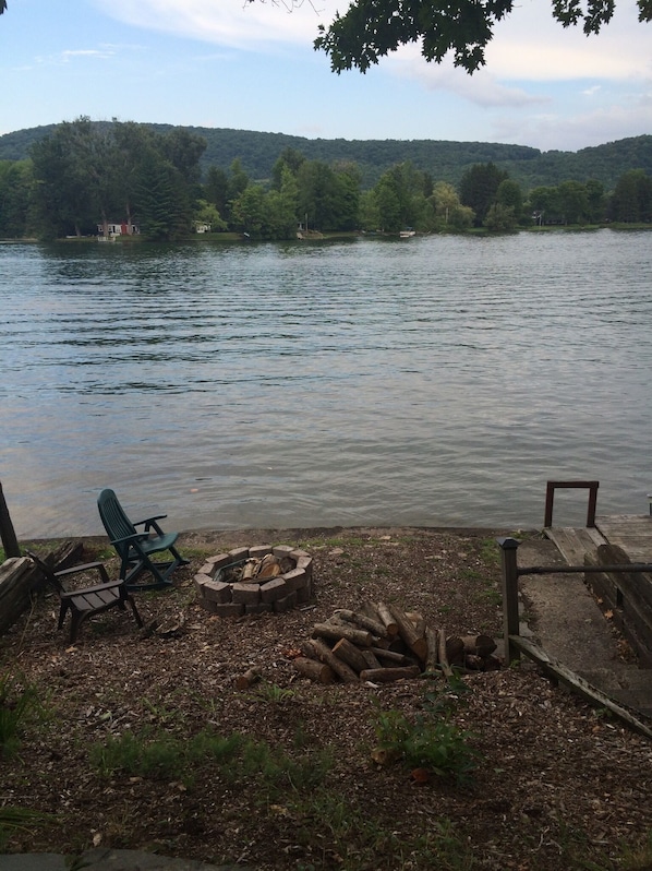 Vista al lago con un muelle, una fogata y asientos al aire libre.