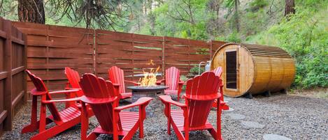 A wooden deck with red Adirondack chairs, a fire pit, and a wooden barrel.