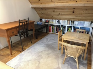 Un angolo lettura accogliente con una scrivania in legno, una sedia, un tavolino e una libreria piena di libri.