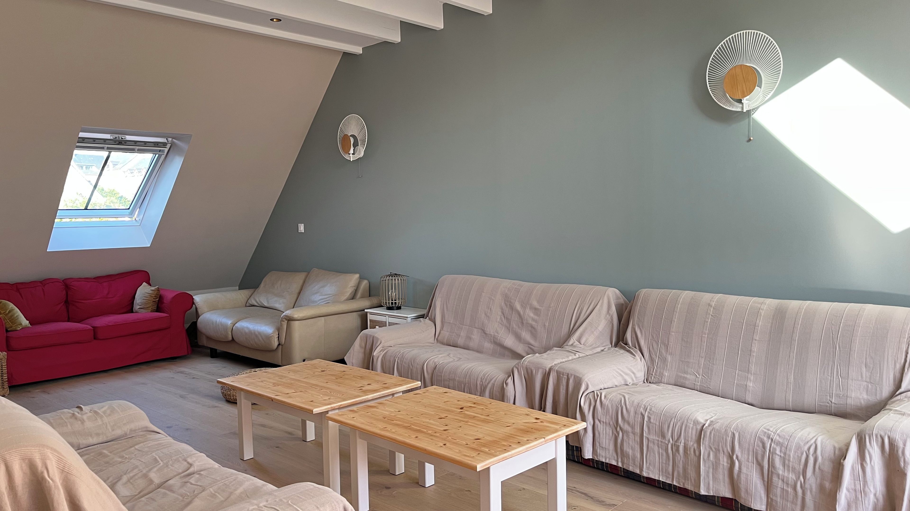 Un salon moderne avec un plafond en pente, un canapé rouge, un canapé beige, une table basse en bois et un lampadaire.