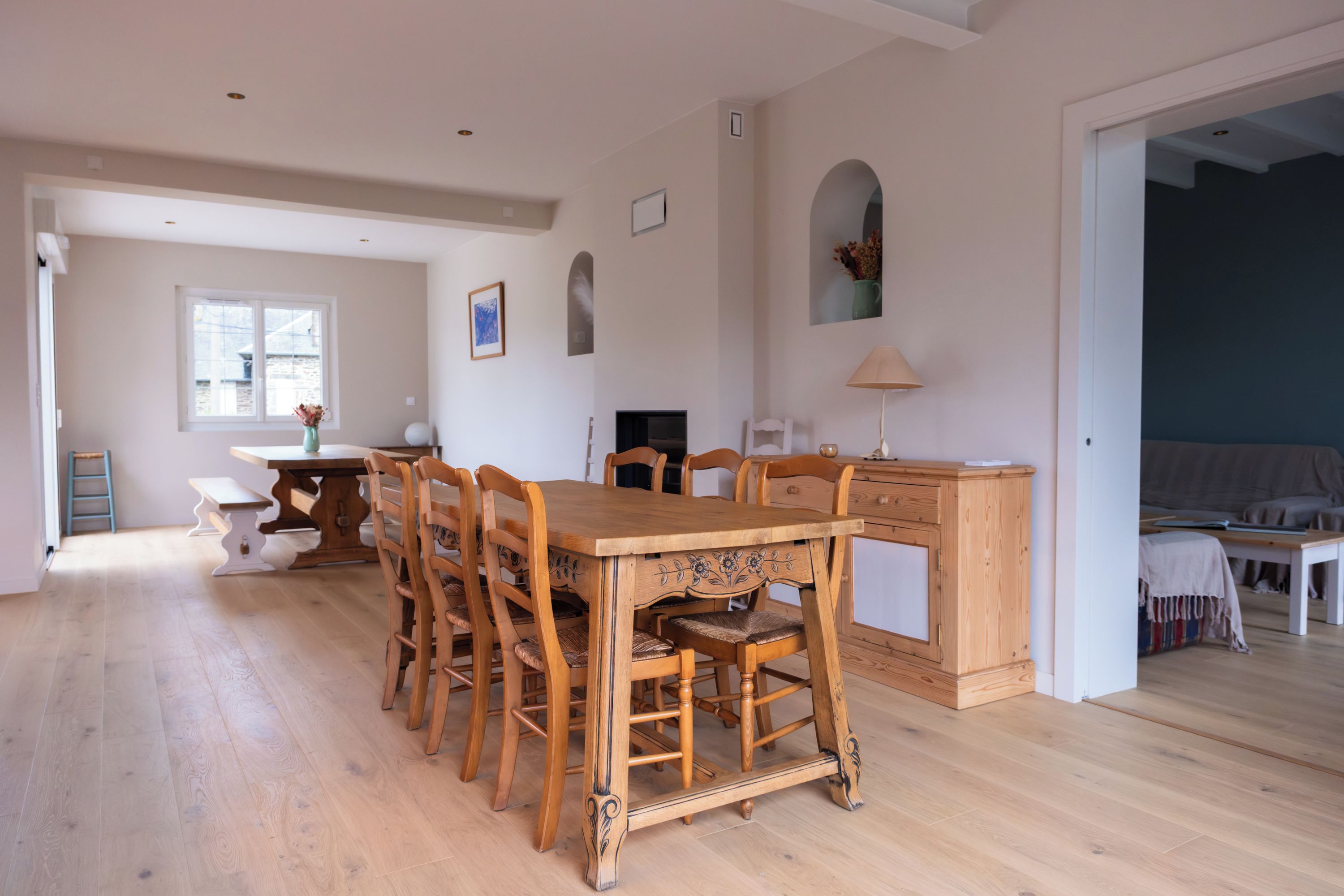 A spacious dining area with a wooden table and chairs, a kitchen area with a stove and cabinets, and a view of the outside through a window.