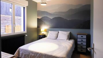 A bedroom with a bed, a nightstand, a lamp, a window, and a wall mural of mountains.