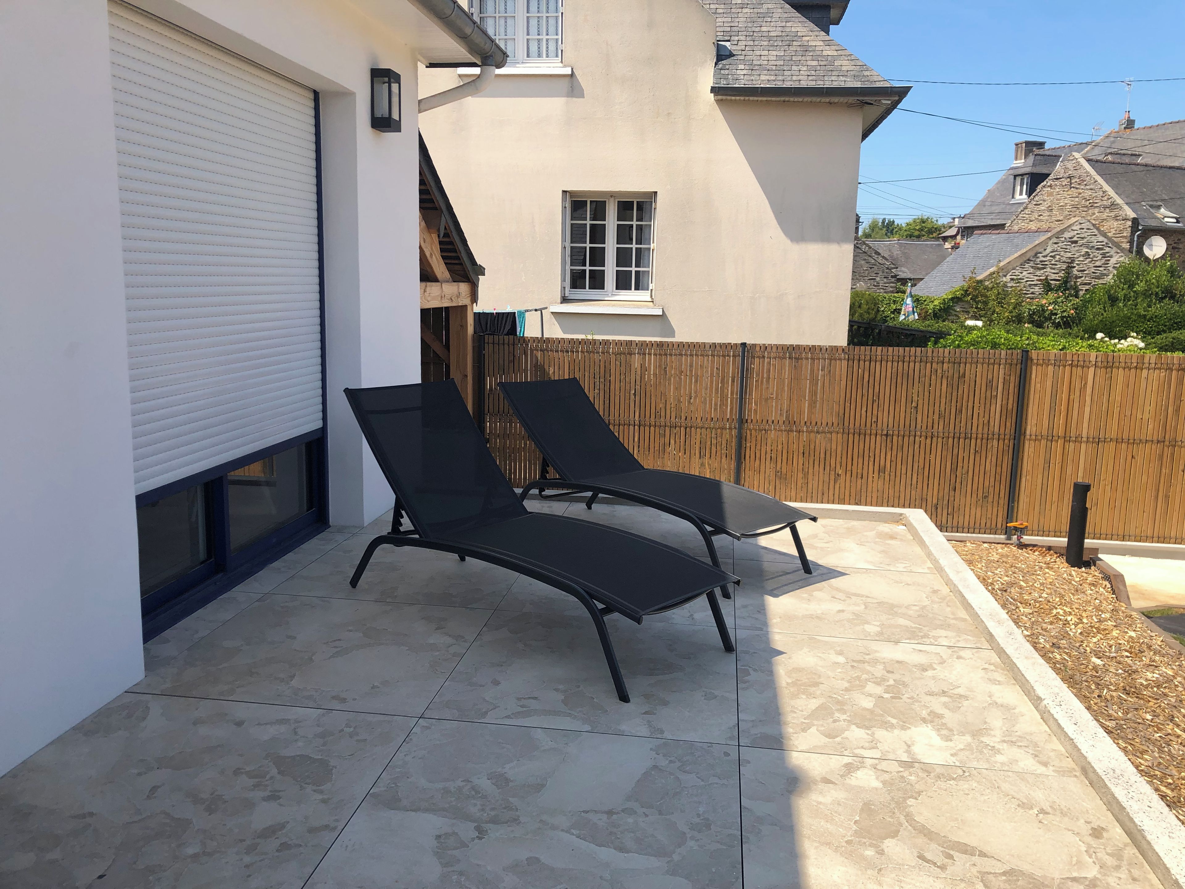 Un patio con dos sillones de descanso, una puerta de garaje blanca y una cerca de madera.