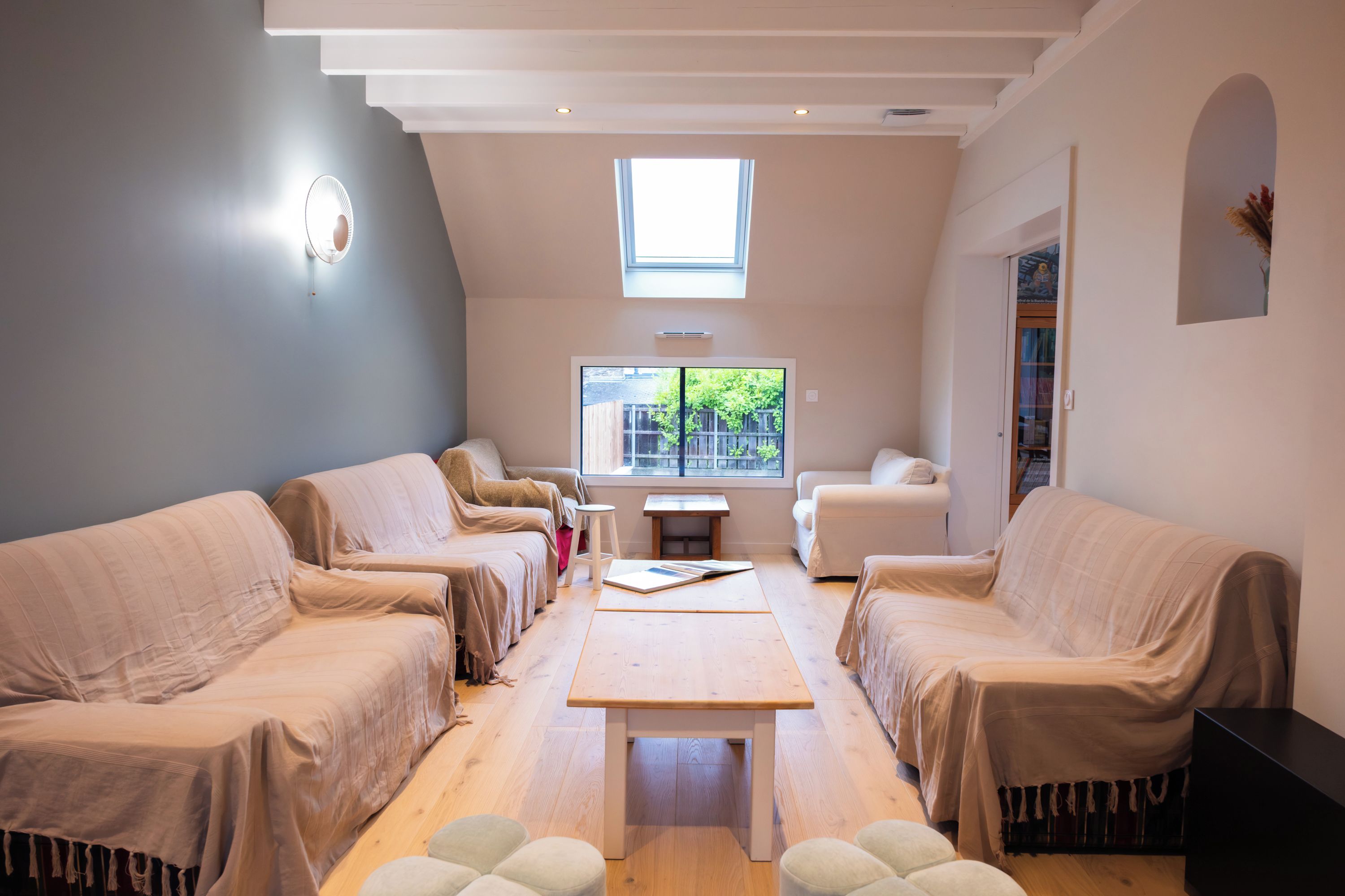 A modern living room with a high ceiling, a skylight, and a view of the outside. There are two sofas, a coffee table, and a small side table.