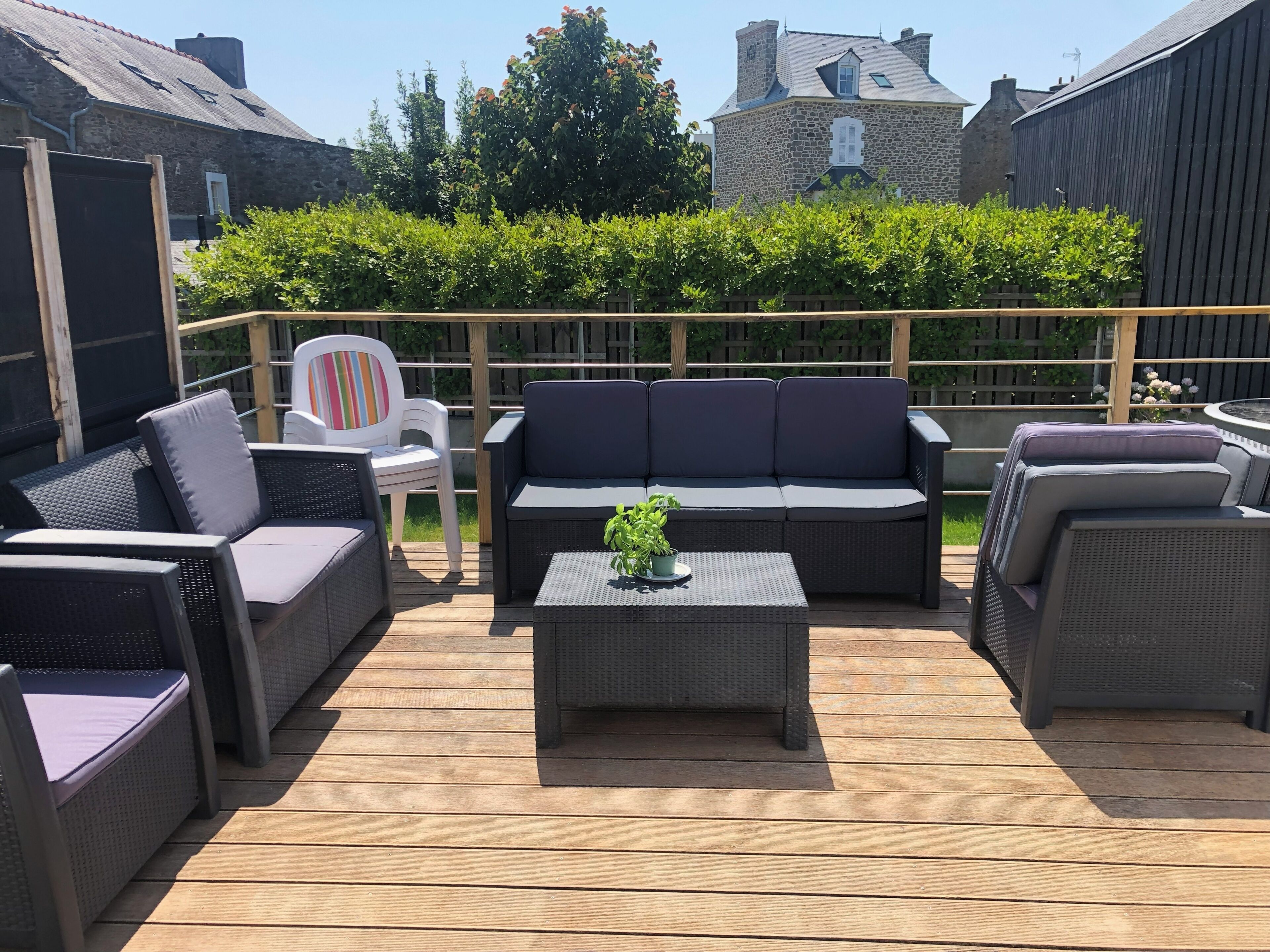 Une terrasse extérieure avec des meubles en osier, une chaise blanche et une petite table agrémentée d’une plante.