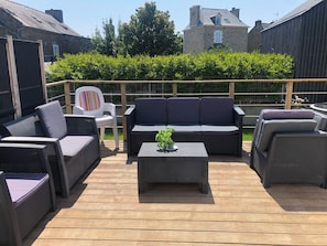 Un patio al aire libre con mobiliario de mimbre, una silla blanca y una pequeña mesa con una planta.
