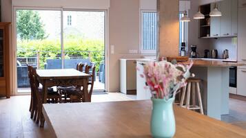 A modern kitchen with a dining area, a large window, and a view of greenery outside.