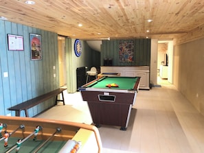 Una mesa de billar junto a una mesa de fútbolín en una sala con paneles de madera y techo con vigas de madera.