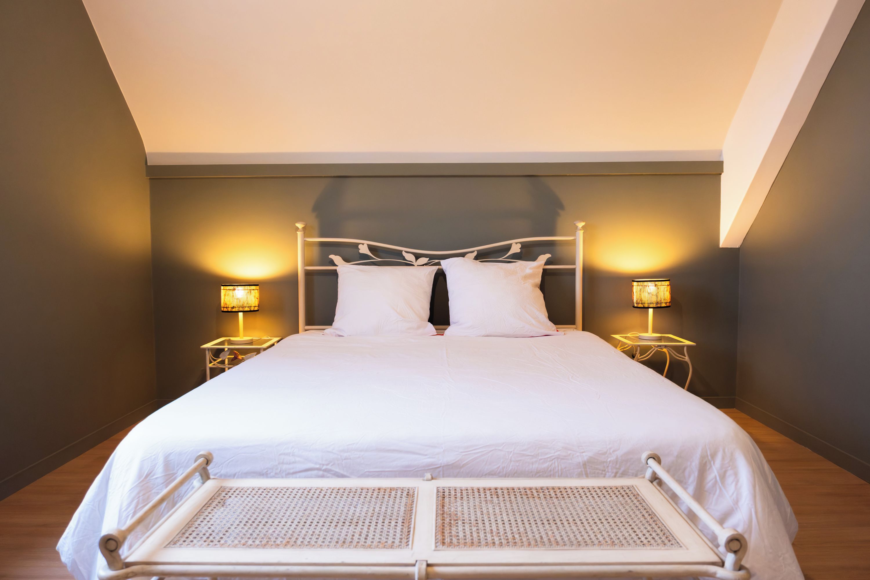 A bed with a white headboard, two bedside lamps, and a wooden floor.