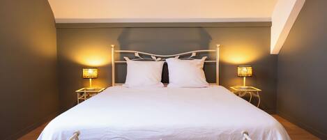 A bed with a white headboard, two bedside lamps, and a wooden floor.