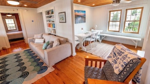 A cozy living room with a sofa, a wooden coffee table, and a patterned rug. There is a bookshelf filled with books and a painting on the wall. - Classic Pawleys. Just Renovated. Long, breezy porches. Steps to beach and creek. (Pawleys Island)