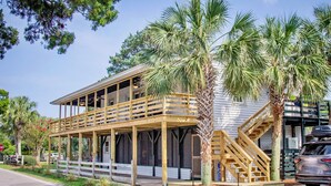 A two-story wooden building with a covered porch, palm trees, and a staircase leading to an upper level. - Classic Pawleys. Just Renovated. Long, breezy porches. Steps to beach and creek. (Pawleys Island)