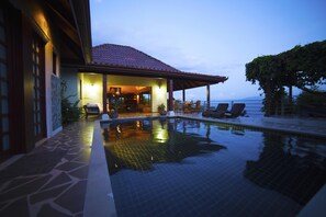 Área da piscina com espaço coberto para sentar e vista para o mar.