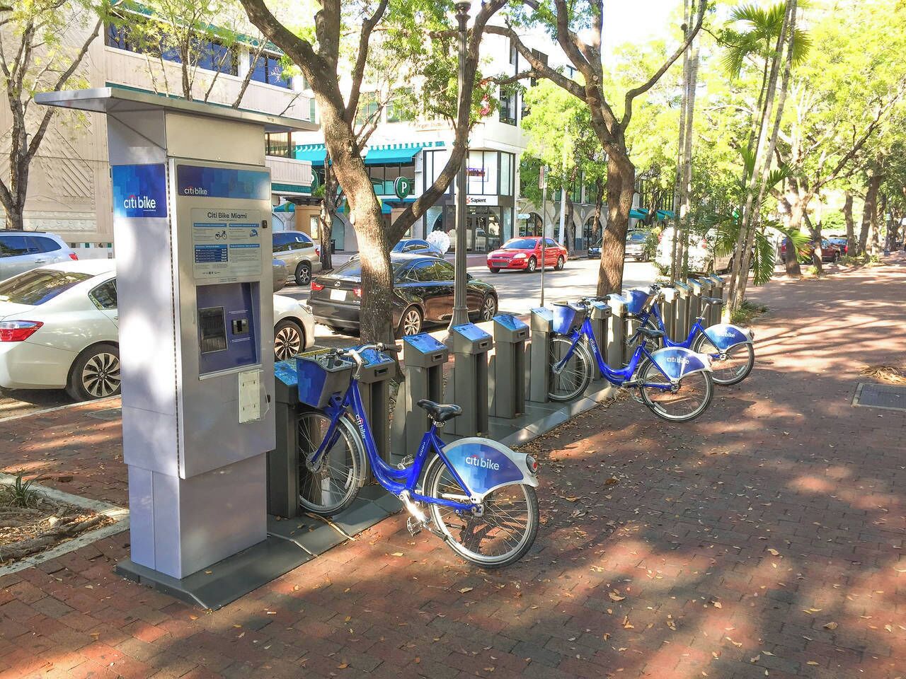 A Citi Bike station with several bicycles parked, a parking meter, and a building with a blue awning in the background.