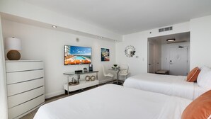 Habitación de hotel con dos camas, televisión, escritorio con lámpara y una mesita con planta.