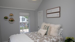 A bedroom with a bed, a window, and a wall with framed text.