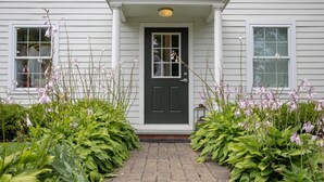 A house with a black front door, white siding, and a brick pathway leading to the entrance.