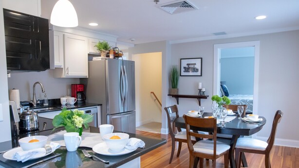 A modern kitchen with a central island, dining area with wooden chairs, and a view of the outdoors.