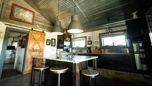 Une cuisine dotée d’un grand îlot central, de tabourets de bar, de luminaires suspendus et d’appareils électroménagers en acier inoxydable.