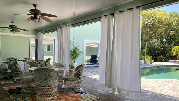 Un espace intérieur spacieux, aménagé avec des meubles en osier, un tapis à motifs et offrant une vue sur une piscine extérieure.
