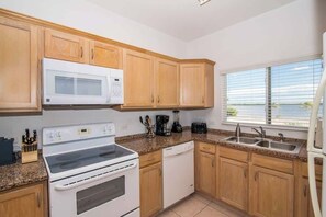 Una cocina con armarios de madera, microondas, estufa, lavavajillas y una ventana con persianas.