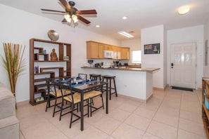 A modern kitchen with wooden cabinets, a dining area with a table and chairs, and a ceiling fan.