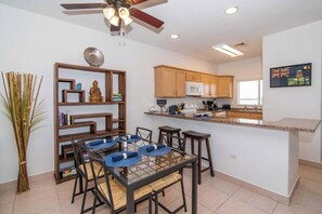 A modern kitchen with wooden cabinets, a microwave, and a dining area with a glass table and chairs. - Waterfront Korner Kai 2BR -- Pool, Jacuzzi & Beachfront Lanai (Cayman Kai)