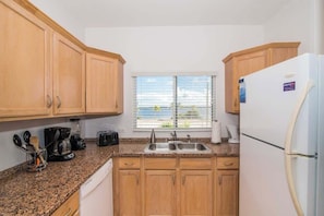 A compact kitchen with wooden cabinets, a granite countertop, a built-in sink, and a refrigerator.
