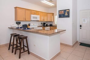 A kitchen with wooden cabinets, a granite countertop, a white microwave, and a flag on the wall.