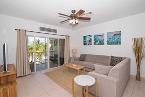 A living room with a sofa, coffee table, and a ceiling fan. There are three framed pictures on the wall and a TV on a stand.