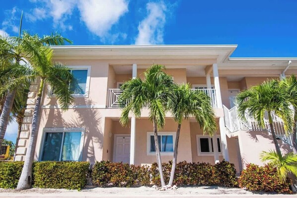 A two-story building with a balcony, palm trees, and a clear blue sky.