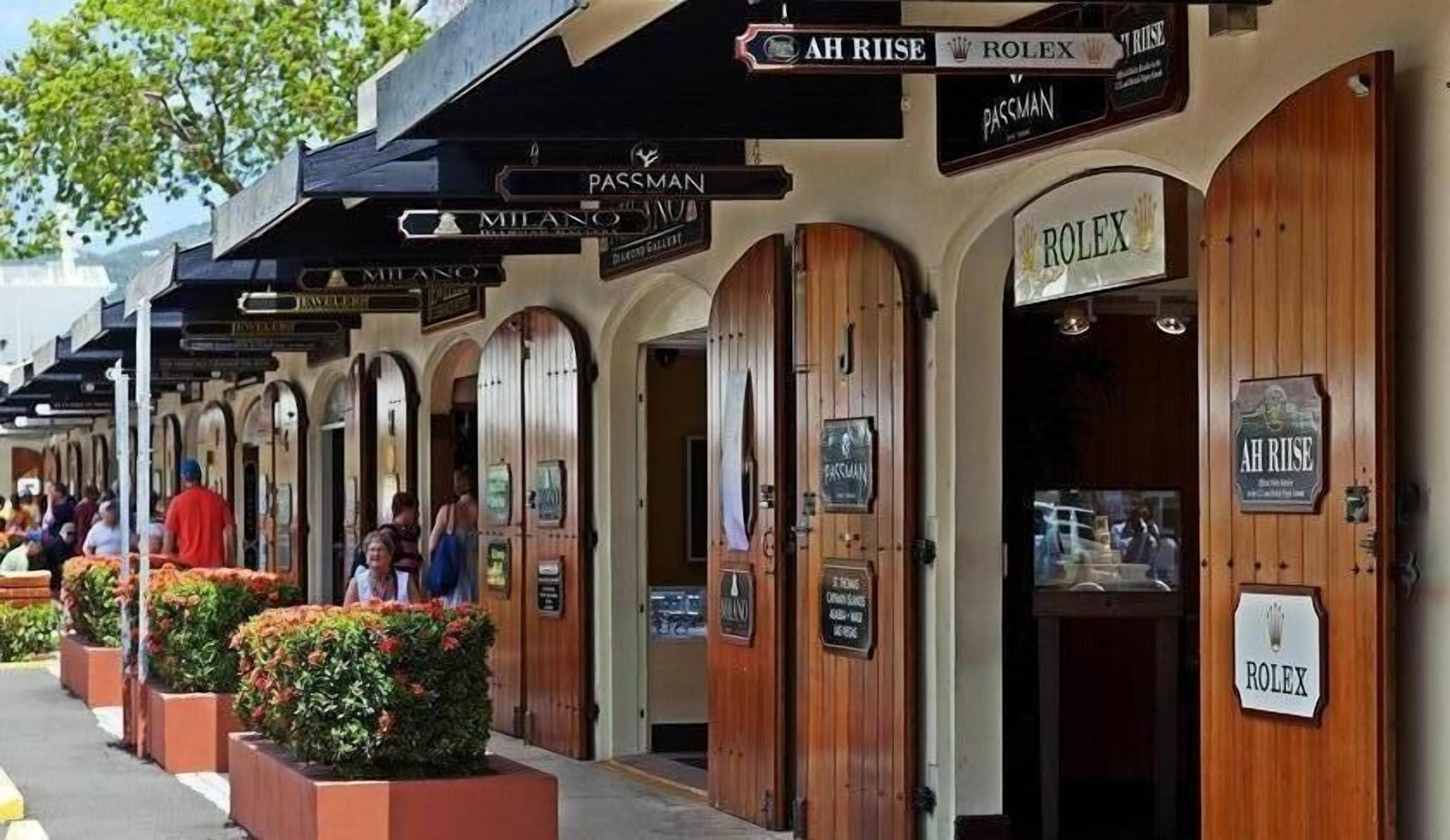 A row of wooden storefronts with signs for brands like AH RISE, ROLEX, and MILANO.
